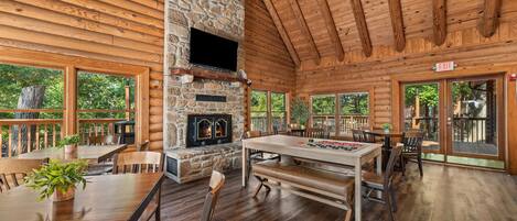 A log cabin interior with a stone fireplace, wooden dining table, and multiple seating arrangements.