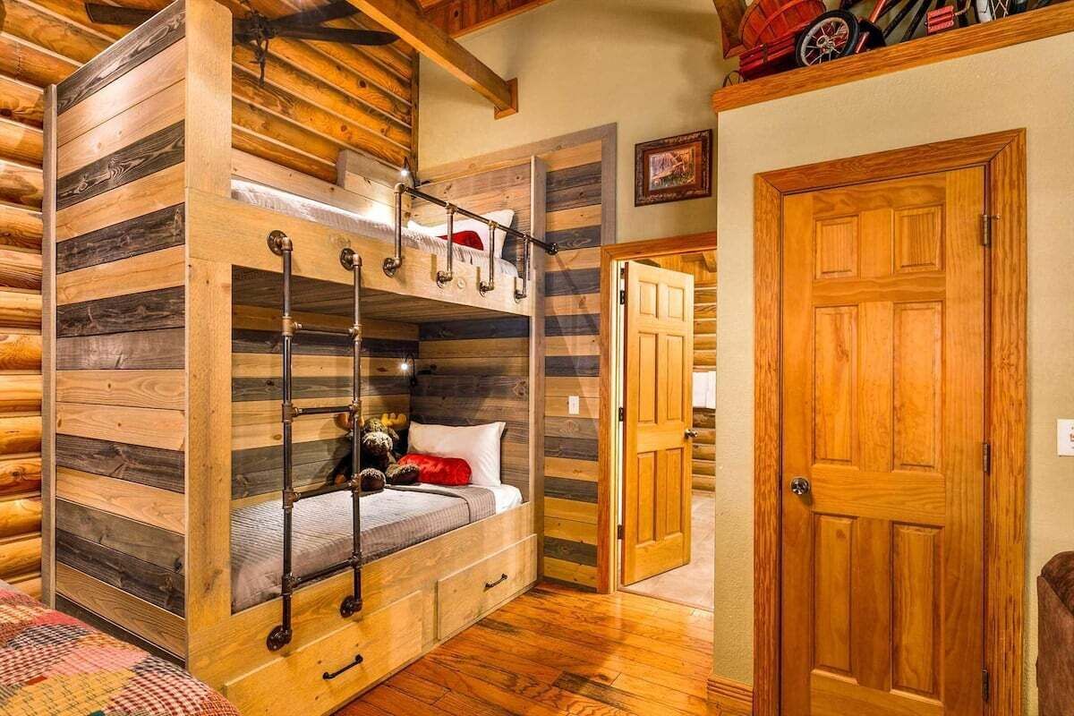 L’intérieur d’une cabane en rondins, avec un lit superposé, des murs en bois, une porte et un escalier.