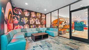A modern lounge area with a curved blue sofa, a wooden coffee table, and a wall adorned with colorful posters.