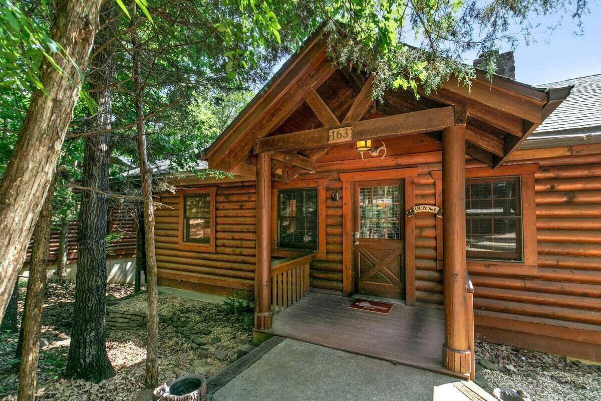 Une cabane en rondins avec un porche, une plaque portant le numéro « 163 » et une pancarte de bienvenue.