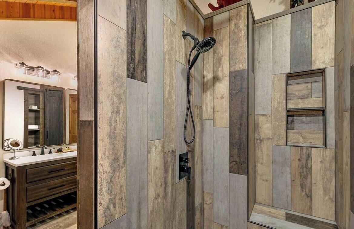 A bathroom with a wooden wall design, a shower with a handheld showerhead, and a vanity with a mirror and sink.