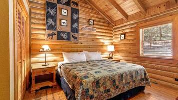 A log cabin bedroom with a bed, two bedside tables, a quilt, and a wall hanging with animal silhouettes.