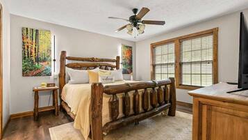 A bedroom with a wooden bed, a desk, and two windows with blinds.