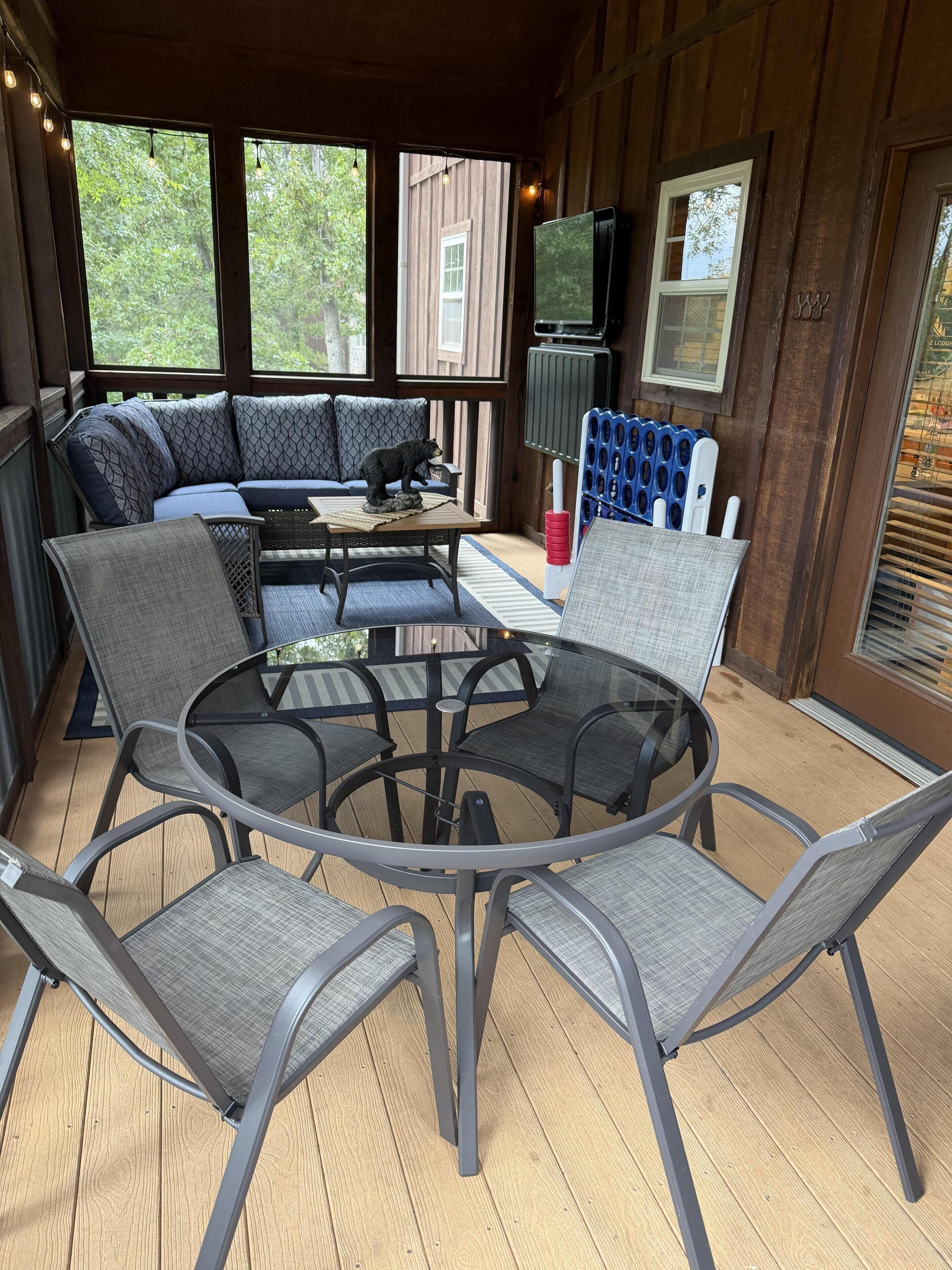 A covered outdoor seating area with a round table and chairs, a sofa with patterned cushions, and a bear statue.