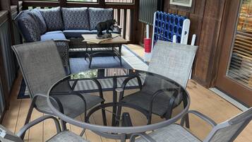A covered outdoor seating area with a round table and chairs, a sofa with patterned cushions, and a bear statue.