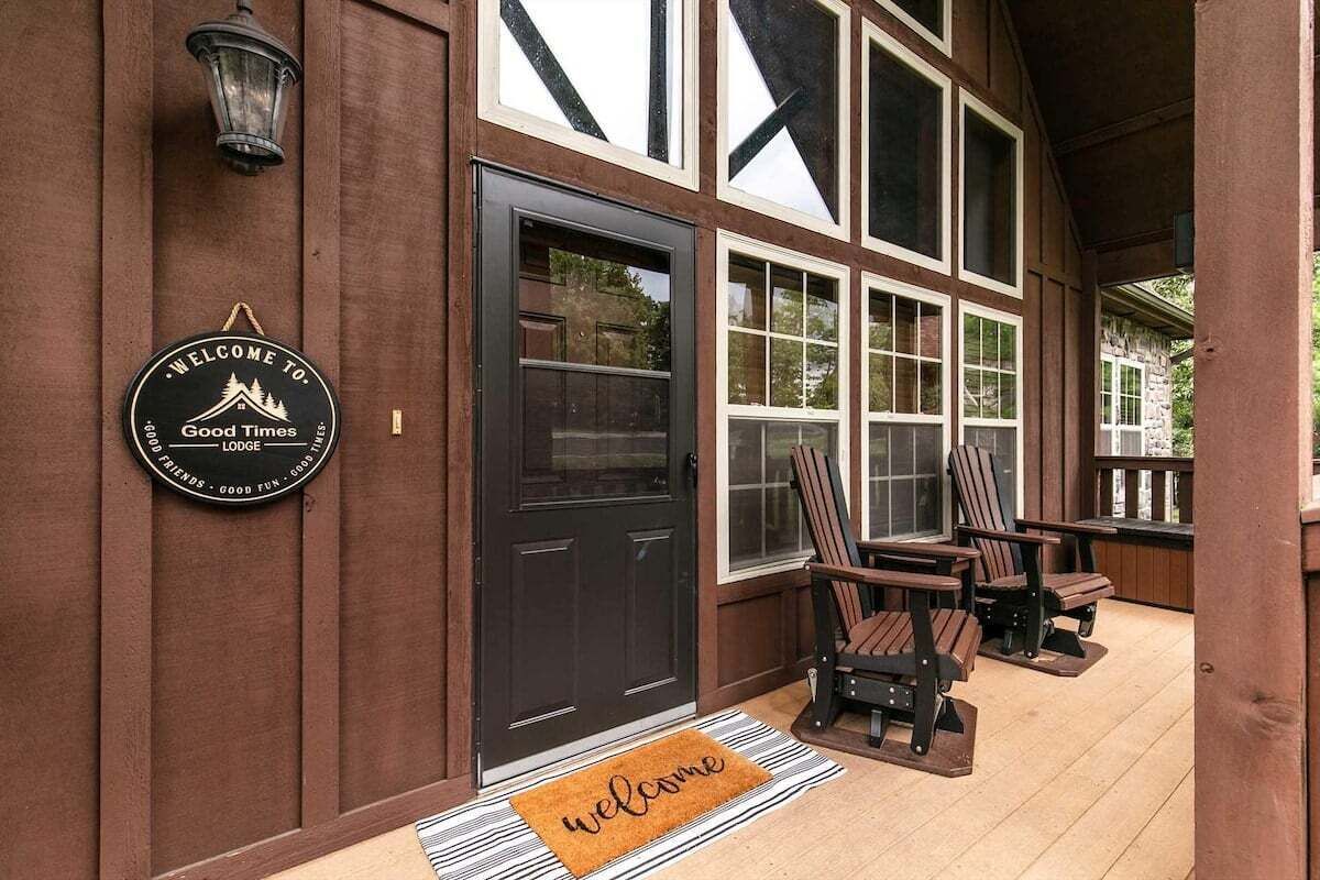 A wooden exterior with a black door, a welcome mat, and two outdoor chairs.