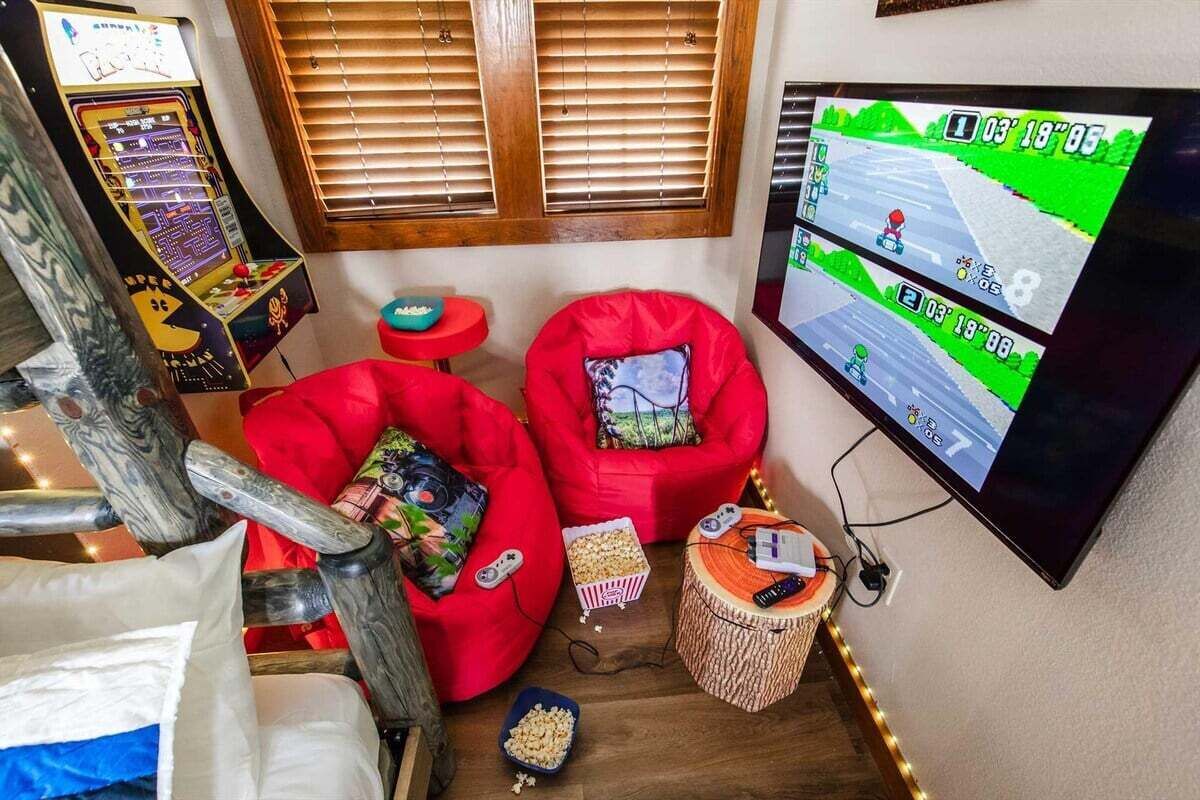 A cozy room with a gaming console, two red bean bag chairs, a TV displaying a racing game, and a small table with snacks.