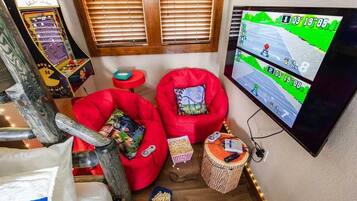 A cozy room with a gaming console, two red bean bag chairs, a TV displaying a racing game, and a small table with snacks.