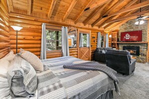 A log cabin interior with a bed, two sofas, a fireplace, and a stone wall. - Genuine Log Cabin_Soaker Tub_Gas Fireplace_Great Location_Free Daily Attraction Tickets (Branson)