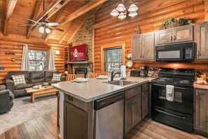 A log cabin interior with a kitchen, dining area, and living room. - Genuine Log Cabin_Soaker Tub_Gas Fireplace_Great Location_Free Daily Attraction Tickets (Branson)