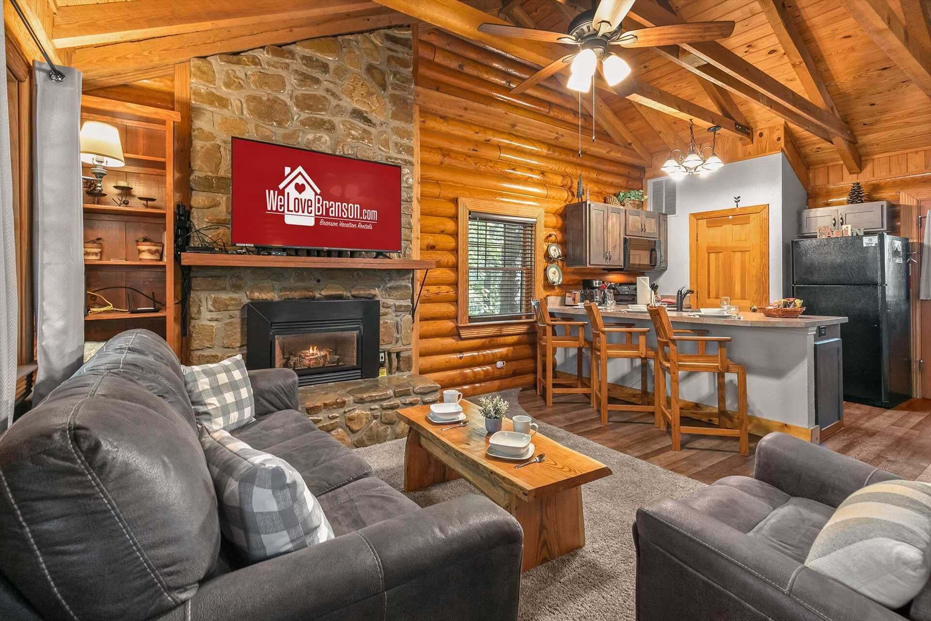 A cozy log cabin interior with a fireplace, a dining area, and a kitchen.