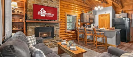 A cozy log cabin interior with a fireplace, a dining area, and a kitchen.