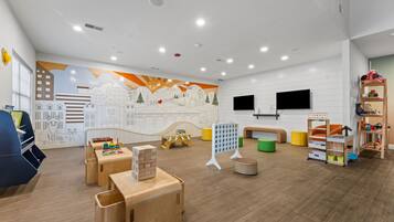 A children's playroom with wooden furniture, a mural, and a television.
