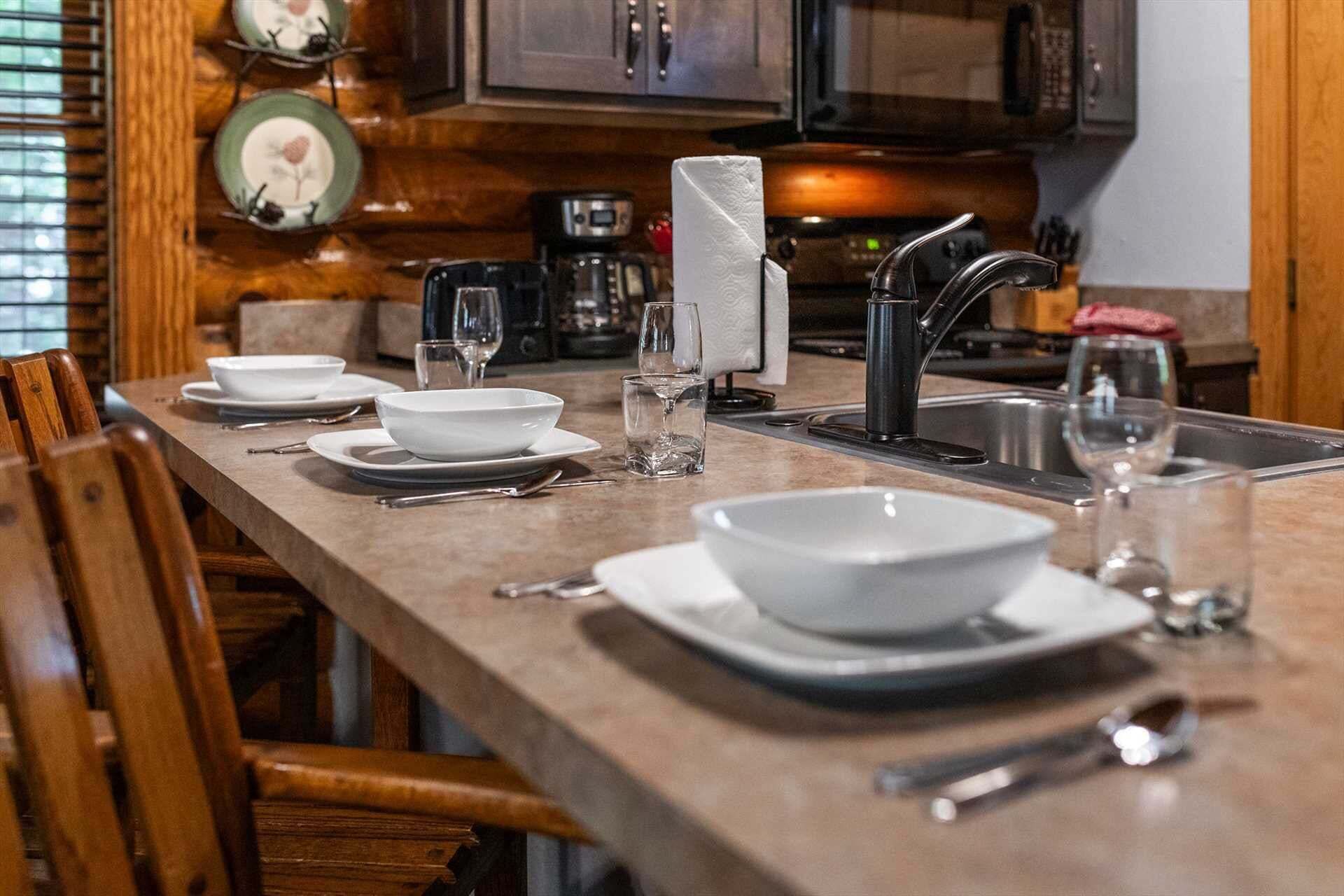 Une table à manger dressée avec de l’assiette blanche, des bols et des couverts, avec un four à micro-ondes et une machine à café en arrière-plan.