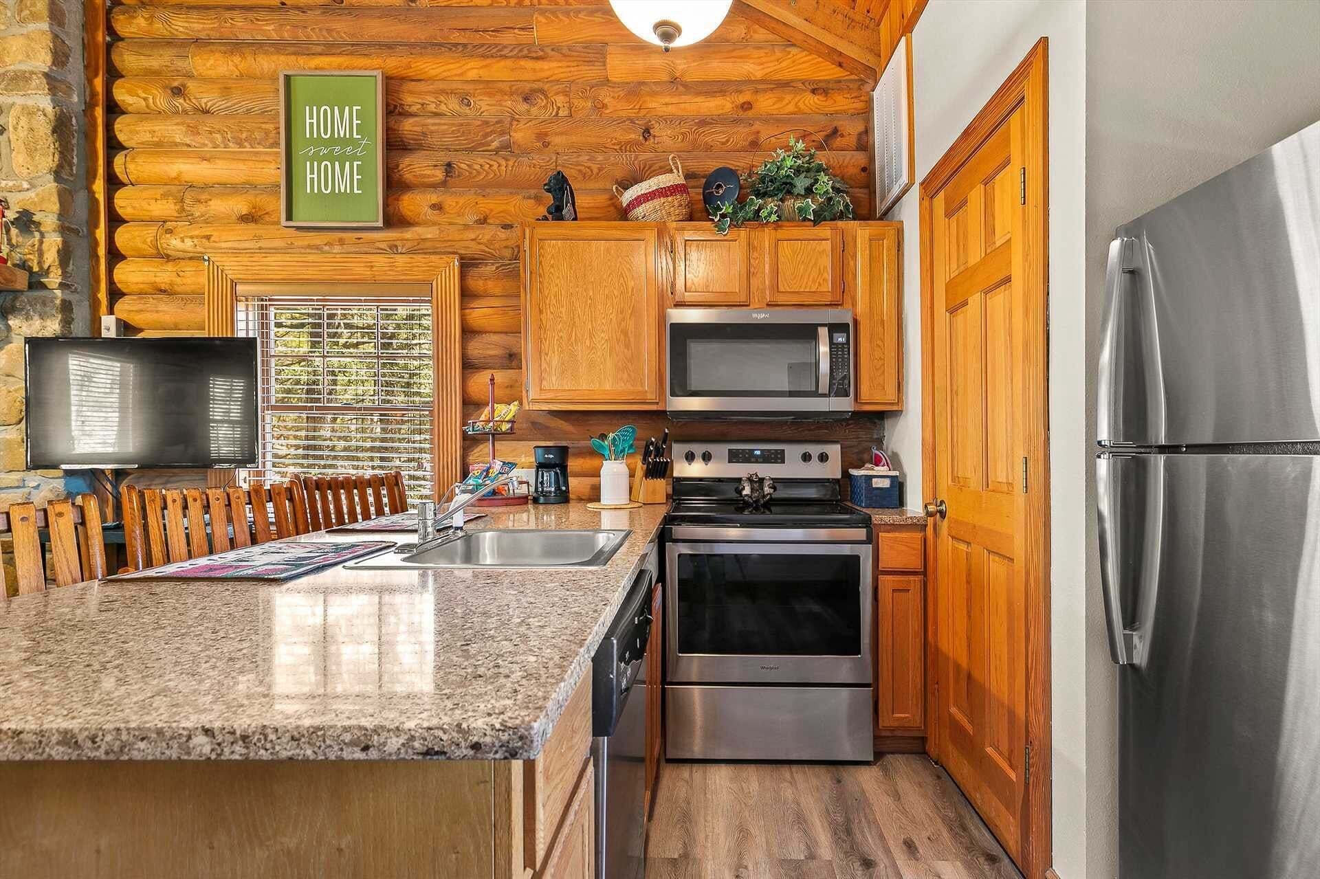 A kitchen with wooden cabinets, a granite countertop, stainless steel appliances, and a television.