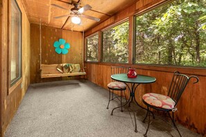 A cozy room with a wooden ceiling, a ceiling fan, a bench, a table with chairs, and large windows offering a view of trees. - Cabin with WhirlpoolTub, King Bed, Washer and Dryer, Gated Community (Branson)