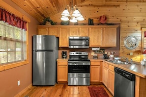 A kitchen with wooden cabinets, stainless steel appliances, and a red rug. - Cabin with WhirlpoolTub, King Bed, Washer and Dryer, Gated Community (Branson)