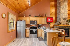 A kitchen with wooden cabinets, stainless steel appliances, a stone fireplace, and a clock on the wall. - Beautiful Wooded Views, Endless Amenities, Free Dailly Attraction Tickets (Branson)