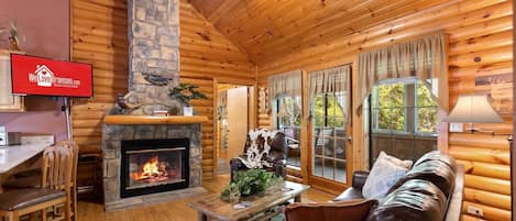 Interior de una cabaña de troncos con chimenea de piedra, mobiliario de madera y un televisor mostrando 'We Love Branson.com'.
