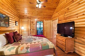 Ein Blockhauszimmer mit Bett, Fernseher auf einer Holzkommode und Deckenventilator.