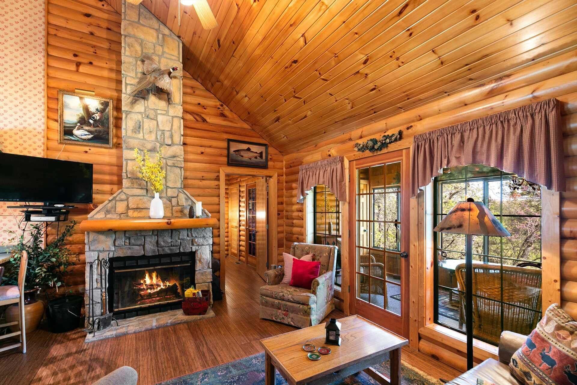 A log cabin interior with a stone fireplace, wooden walls, a television, and a cozy seating area.
