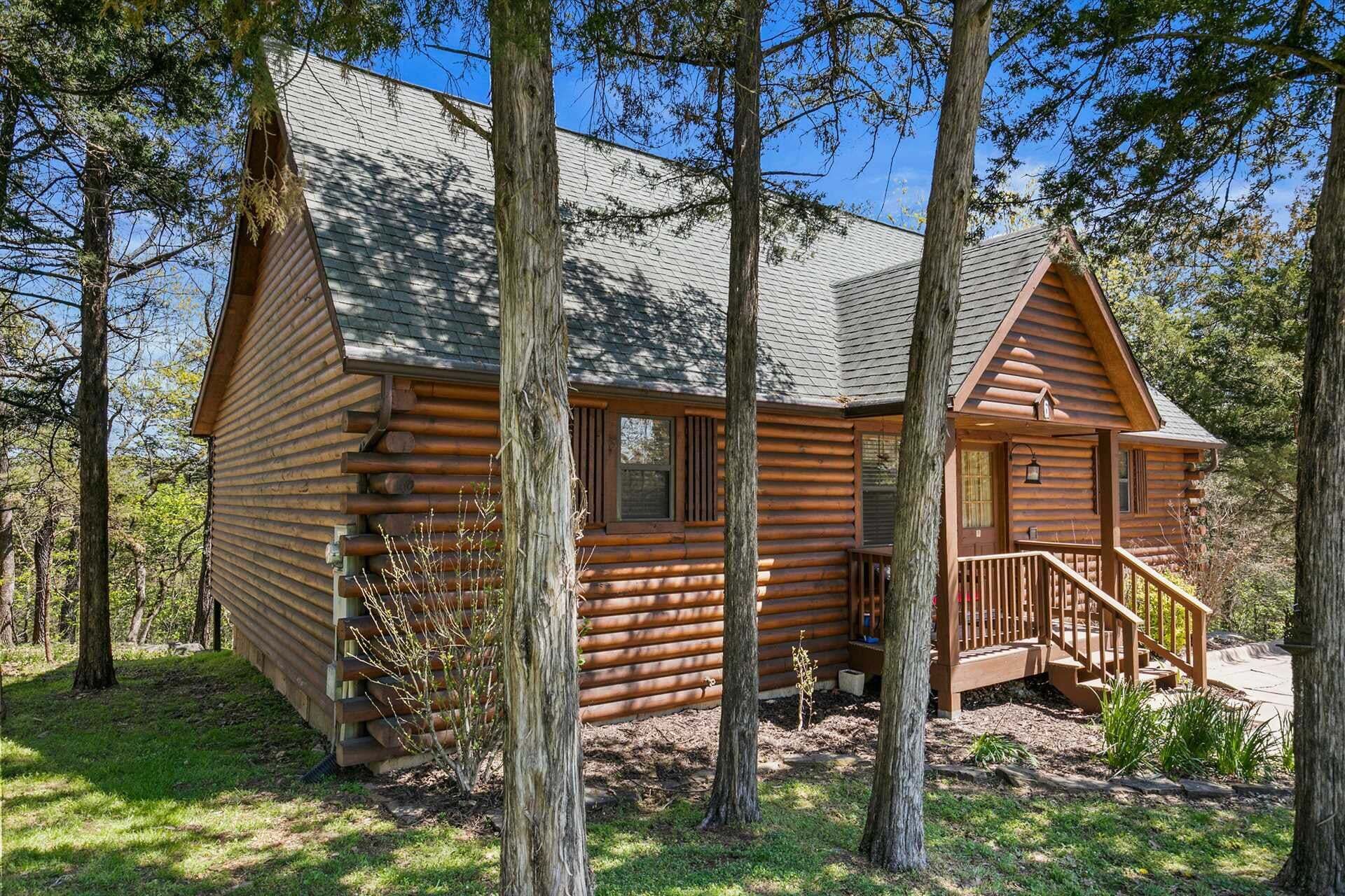 A log cabin with a porch and a staircase, surrounded by trees.
