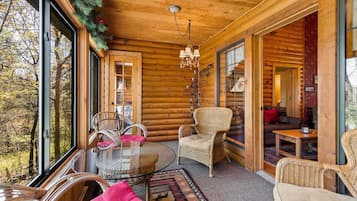 A log cabin interior with a glass door leading to a forest view, wicker furniture, and a chandelier.
