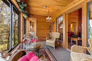 A log cabin interior with a glass door leading to a forest view, wicker furniture, and a chandelier.