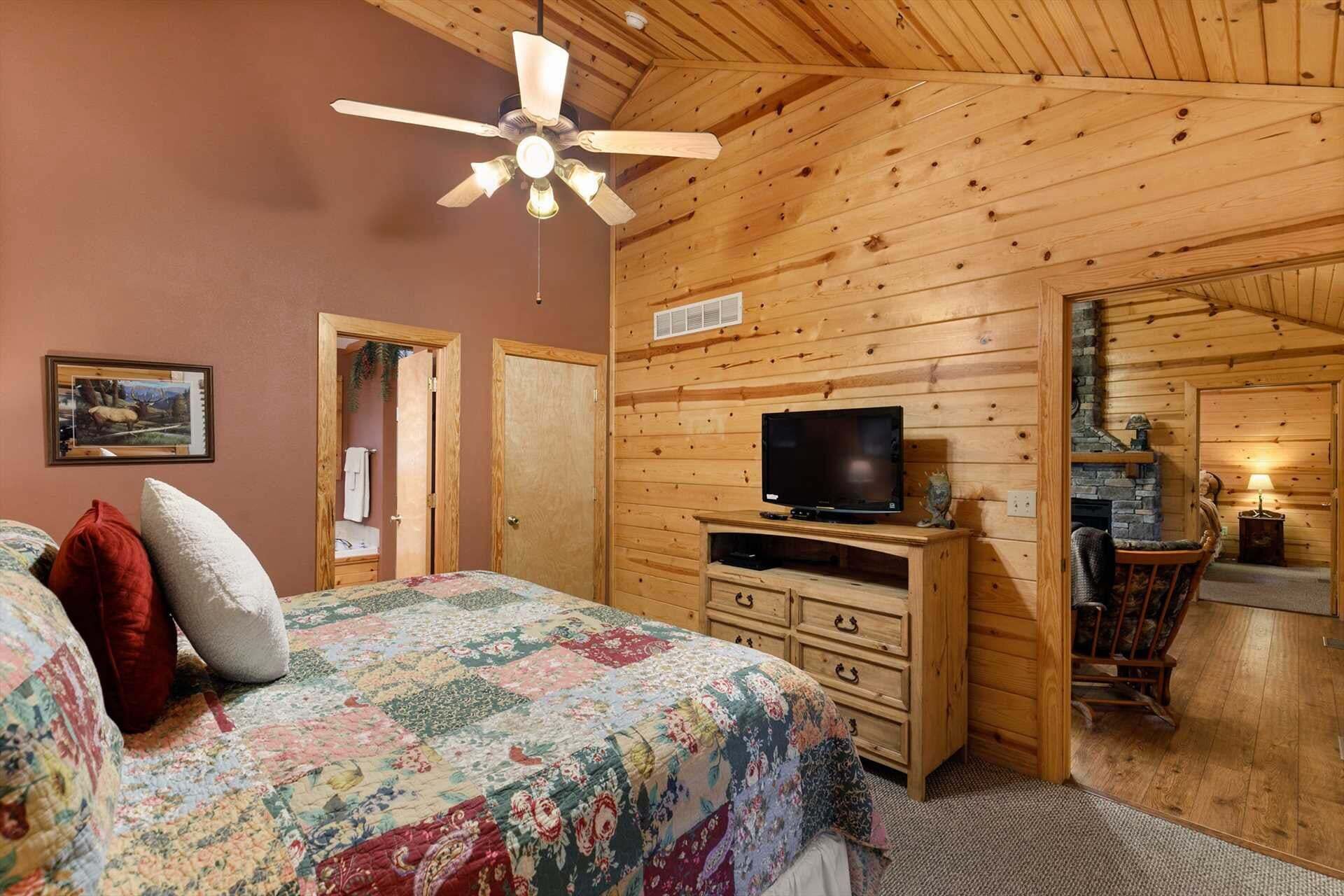 A bedroom with a bed, a television, a fireplace, and a ceiling fan.