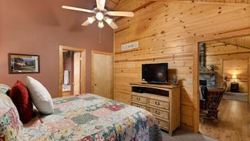 A bedroom with a bed, a television, a fireplace, and a ceiling fan.