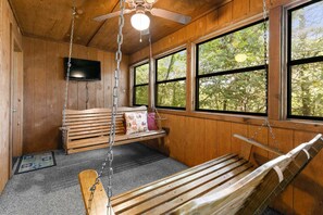 A wooden interior with a swing bed, large windows, and a ceiling fan. - Beautiful Wooded Views, Screened-In Porch, Free Daily Attraction Tickets (Branson)