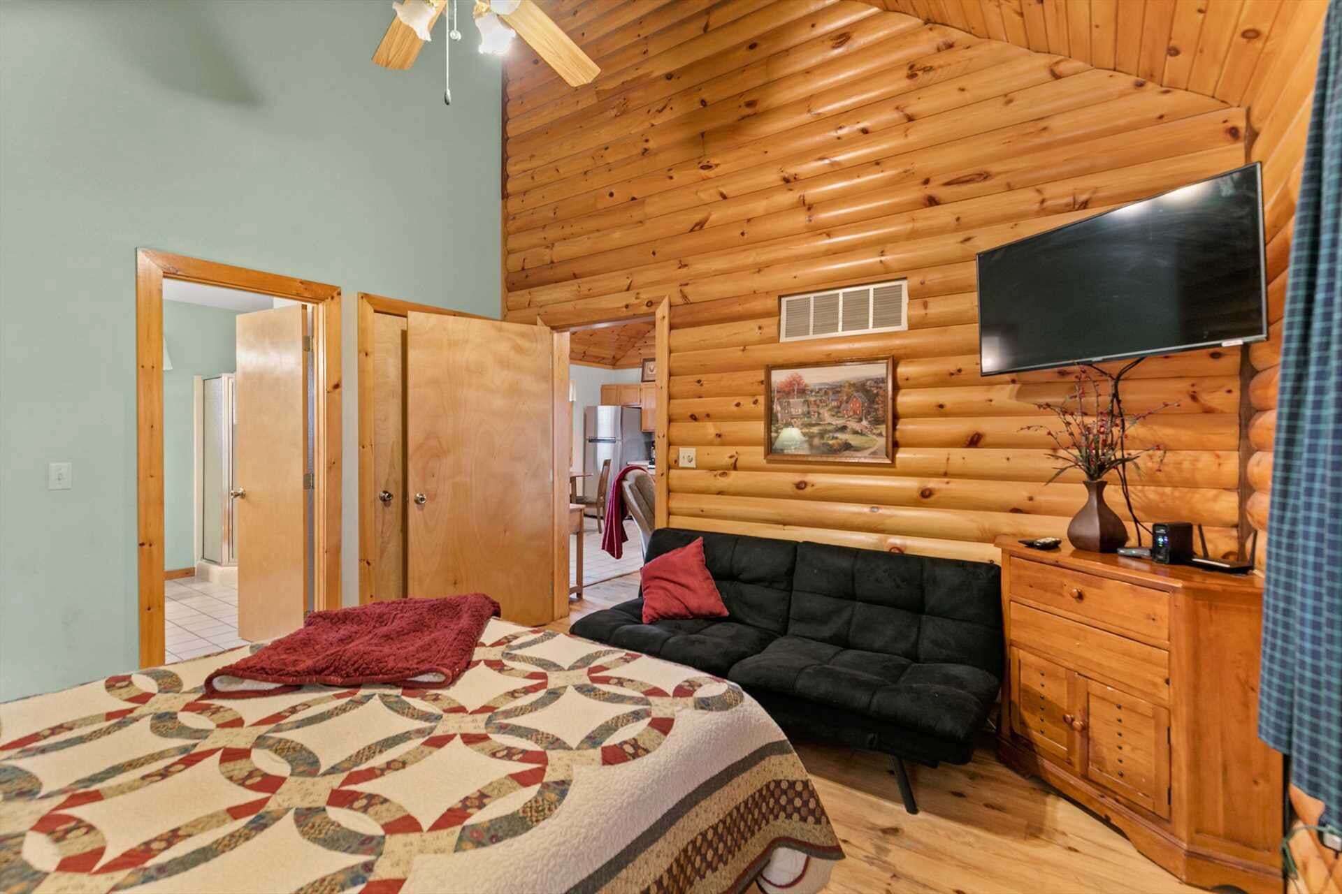 Interior de una cabaña de troncos con cama, sofá, televisión y paredes de madera.