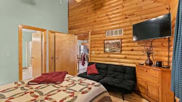 Interior de una cabaña de troncos con cama, sofá, televisión y paredes de madera.