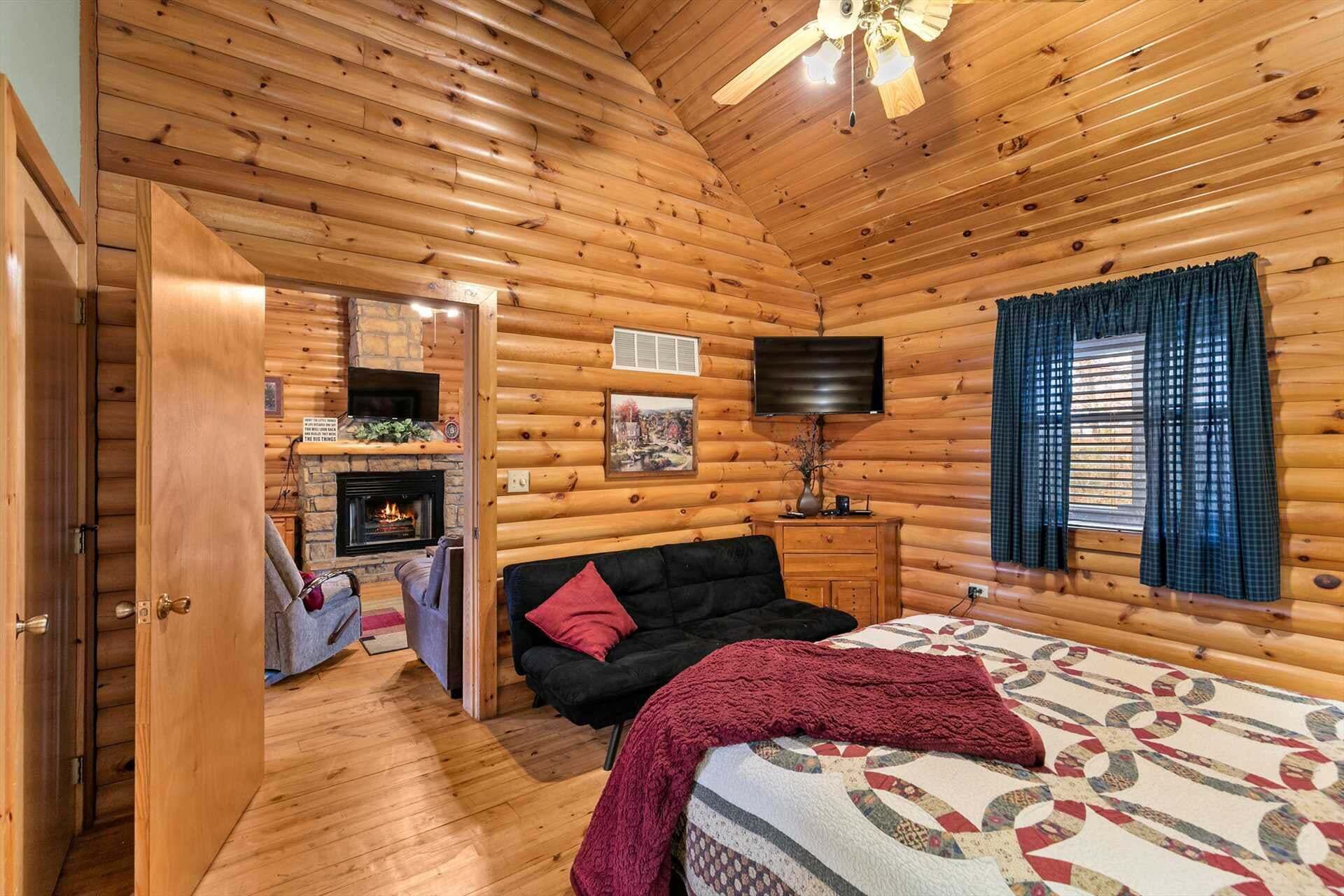 A log cabin interior with a fireplace, a sofa, a bed, and a television.