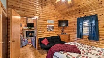 A log cabin interior with a fireplace, a sofa, a bed, and a television.