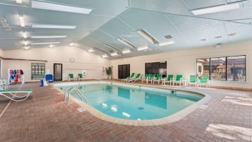 An indoor swimming pool with clear water, surrounded by lounge chairs and a brick floor.