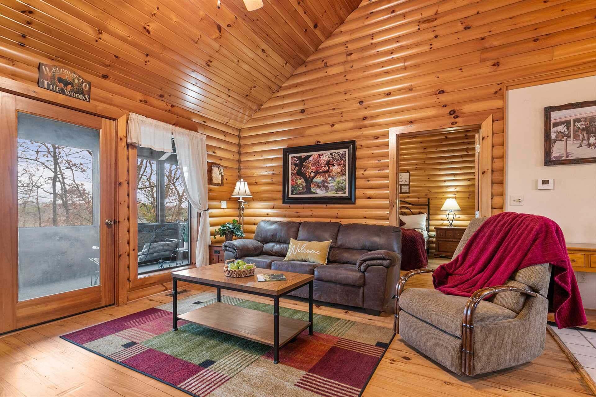 Accogliente interno di una baita in legno, con soffitto in legno, un divano, una poltrona, un tavolo e un quadro incorniciato appeso al muro.