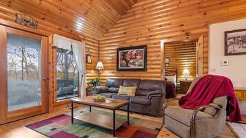 Accogliente interno di una baita in legno, con soffitto in legno, un divano, una poltrona, un tavolo e un quadro incorniciato appeso al muro.