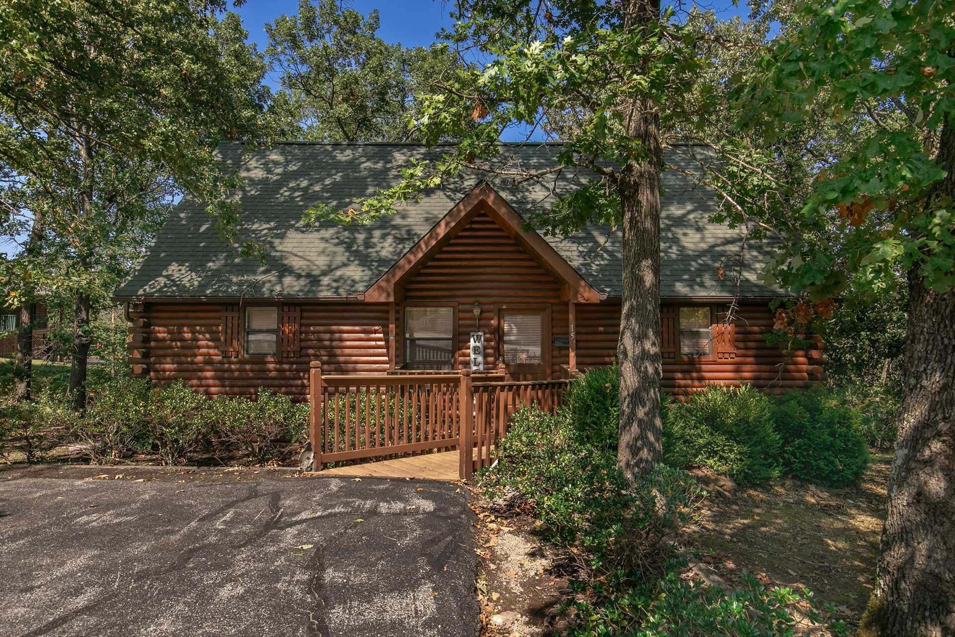 A log cabin with a porch, surrounded by trees.