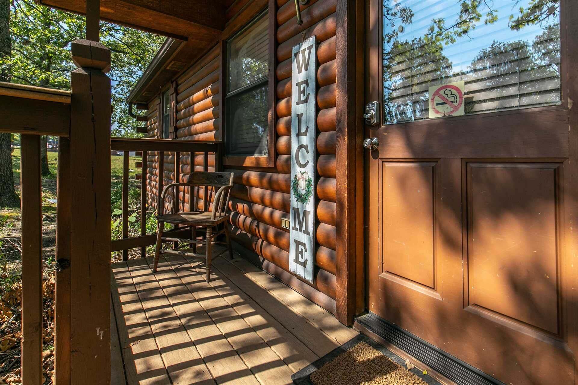 Una cabaña de madera con un porche, un letrero de bienvenida y un cartel de no fumar.