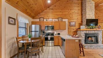 A kitchen with wooden cabinets, a central island, a stone fireplace, and a television mounted above it.