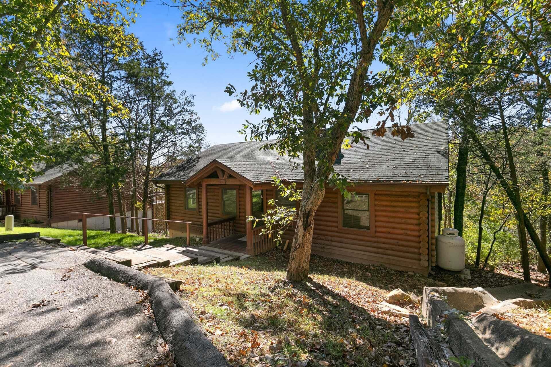 A log cabin with a porch, surrounded by trees and a clear sky.