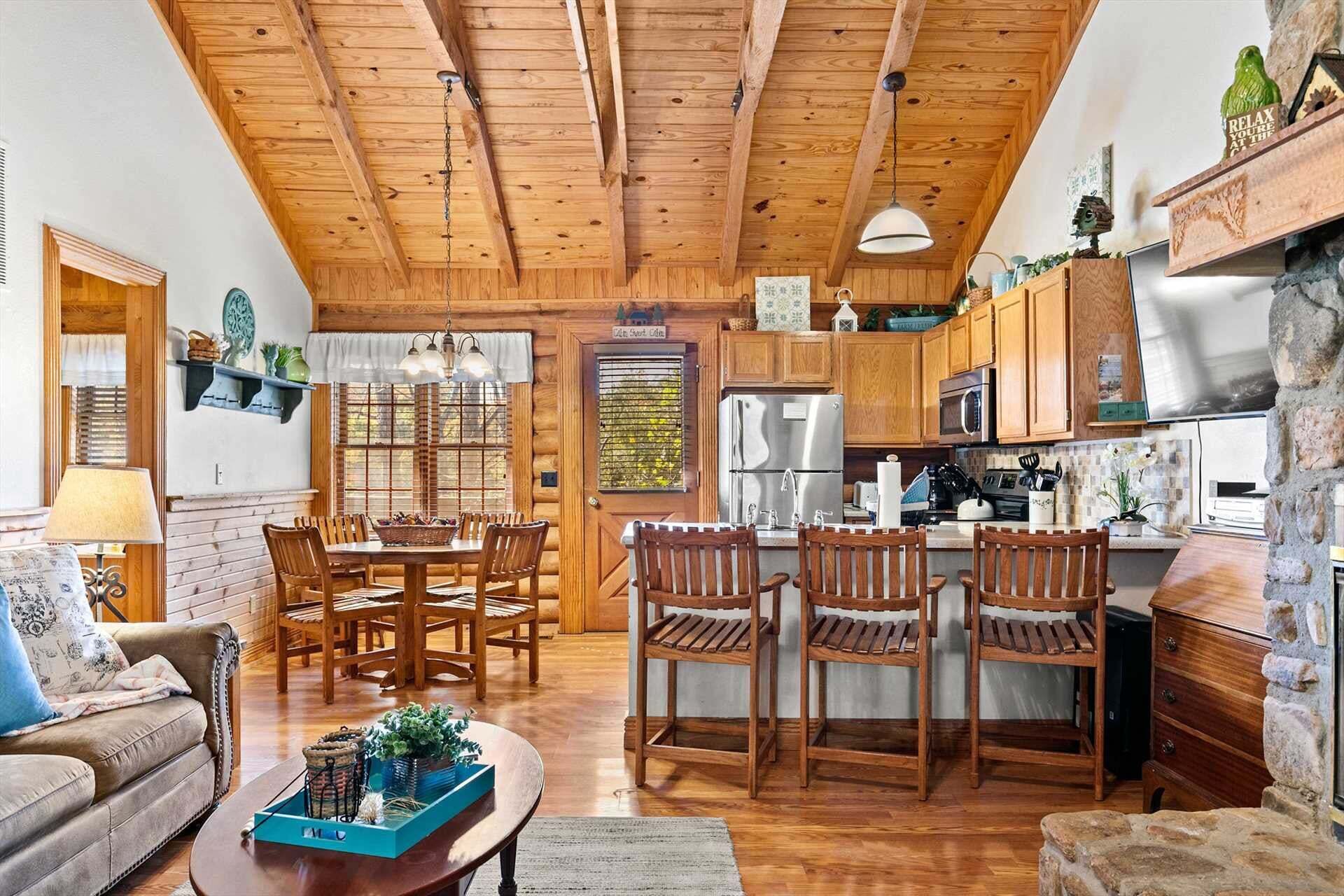 Amplia sala de estar con techo de madera, una mesa de comedor con sillas, una cocina con armarios de madera y electrodomésticos, y una pared de acento de piedra.