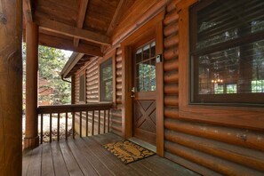 Une cabane en bois avec un porche, une porte dotée d ’une fenêtre et un paillasson.