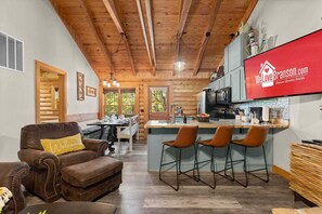 L’intérieur d’une cabane en rondins comprend un coin repas, une cuisine et un salon avec un canapé en cuir.
