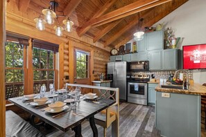 A cabin interior with a dining table set for four, a kitchen with modern appliances, and a television mounted on the wall. - Log Cabin_ Resort Amenities_Free Daily Attraction Tickets (Branson)