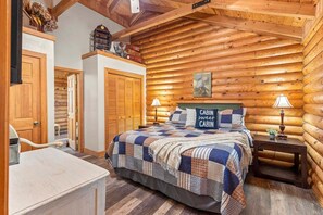 A log cabin bedroom with a bed, bedside lamps, a wooden wardrobe, and a bench. - Log Cabin_ Resort Amenities_Free Daily Attraction Tickets (Branson)