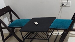 A small black table with a single white object on it, placed between two dark wooden chairs with teal cushions. - Hotel Dream Palace (Luni)