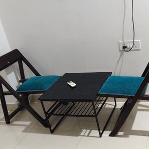 A small black table with a single white object on it, placed between two dark wooden chairs with teal cushions.