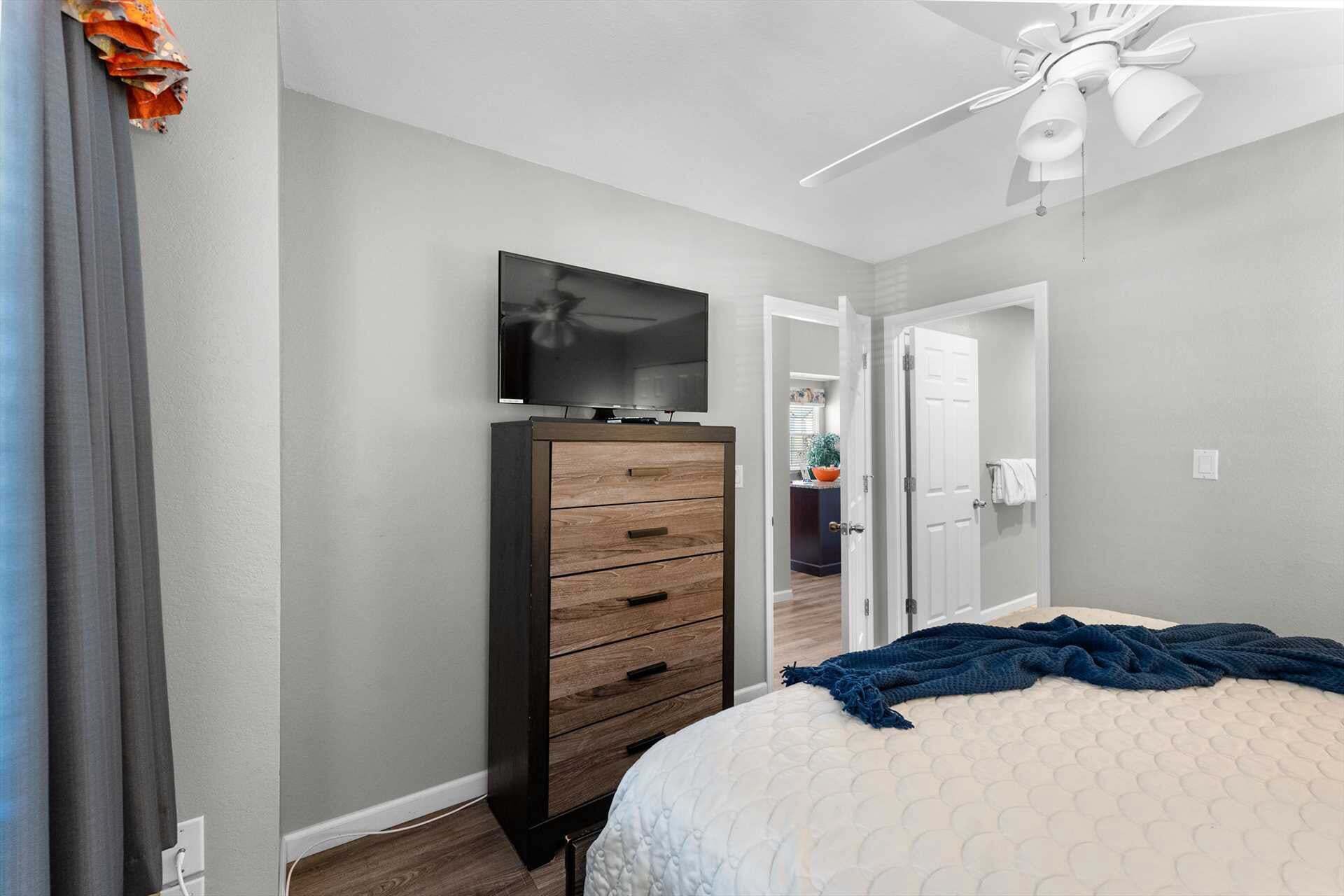 Une chambre à coucher avec un lit, une commode, un téléviseur et un ventilateur de plafond.